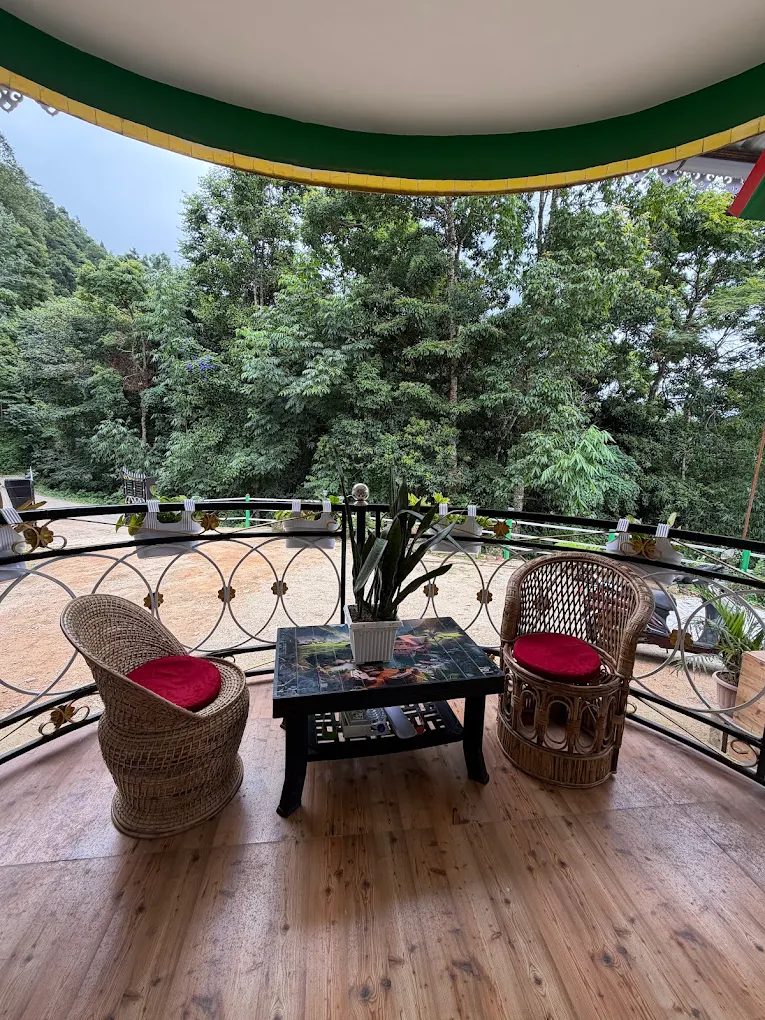 Cane chairs and a table on the forest-facing porch at Kepchaki Stay — an open-air workspace in Lamahatta