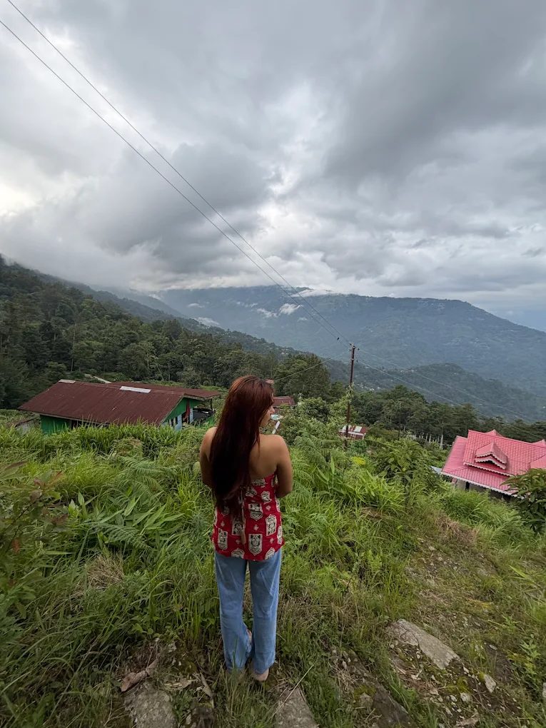 A guest pausing on a village walk above Rana Village, Lamahatta, with cloud over the far ridges